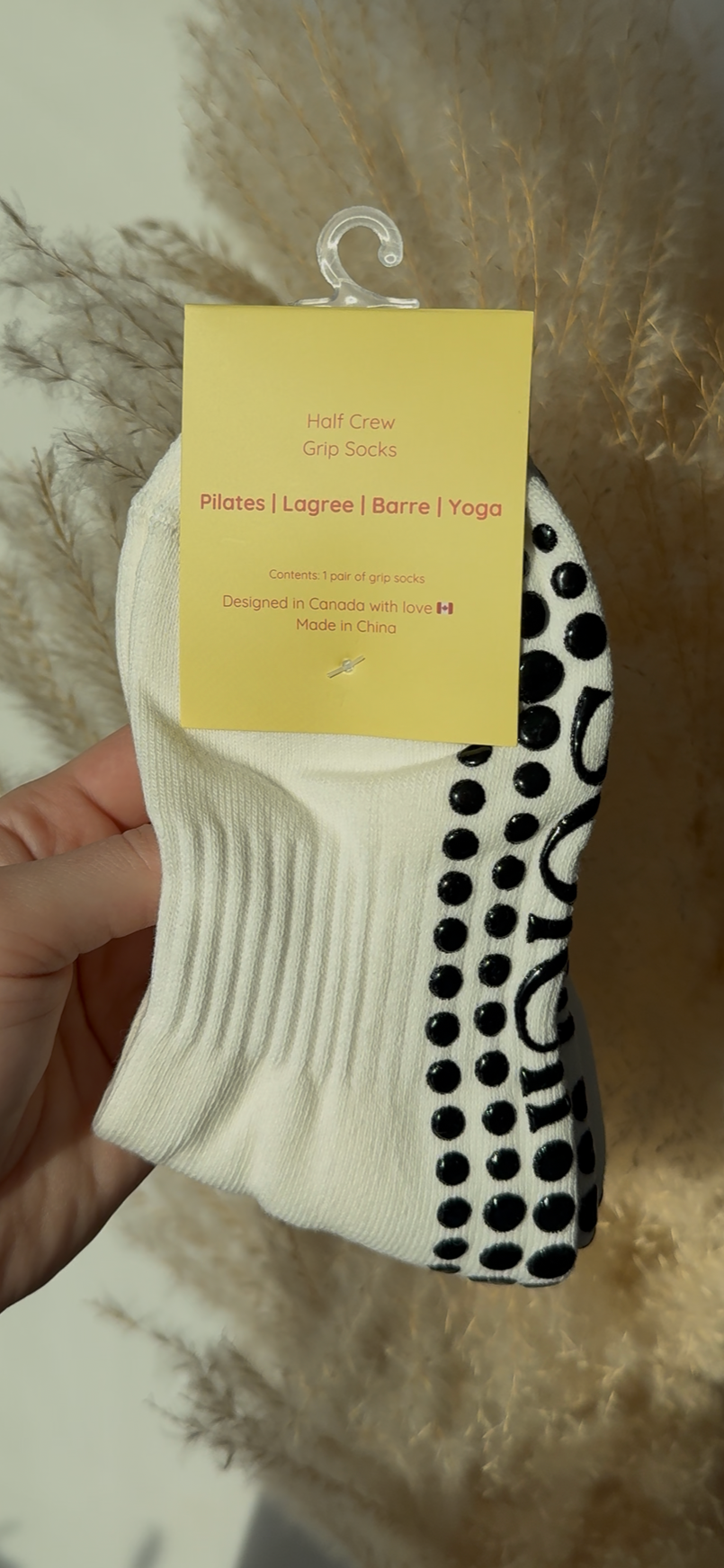 Hand holding a white sock with black grips against a neutral background