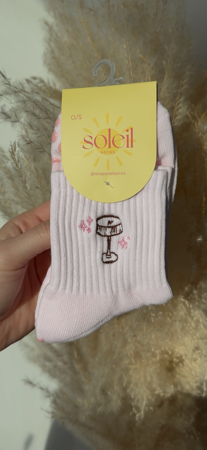 pink sock with pink sole and soleil tag with brown embroidery in shape of espresso martini held against a decorative background