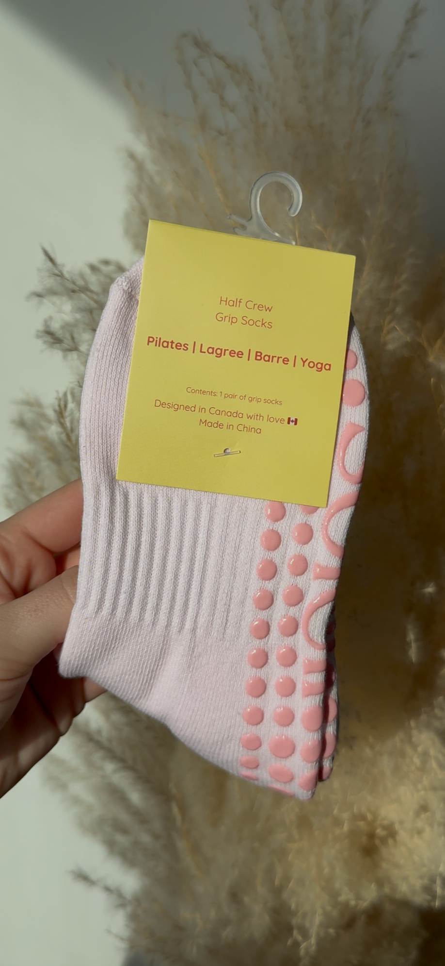 Hand holding a pink sock with a yellow label against a neutral background