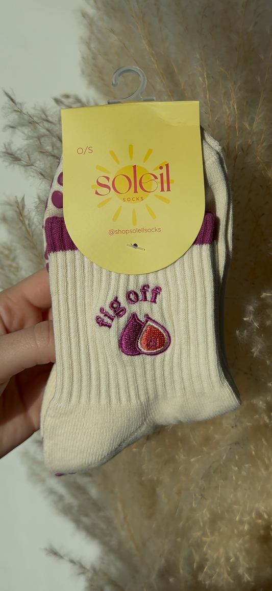 Hand holding a beige sock with a yellow label against a neutral background with fig motif and text saying "fig off"