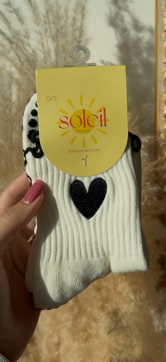 White sock with black heart design held by a hand against a decorative mirror background