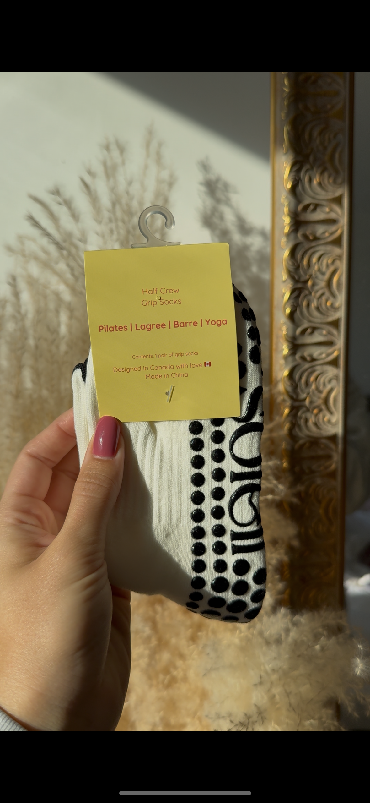 Hand holding a sock with a yellow tag against a decorative mirror background