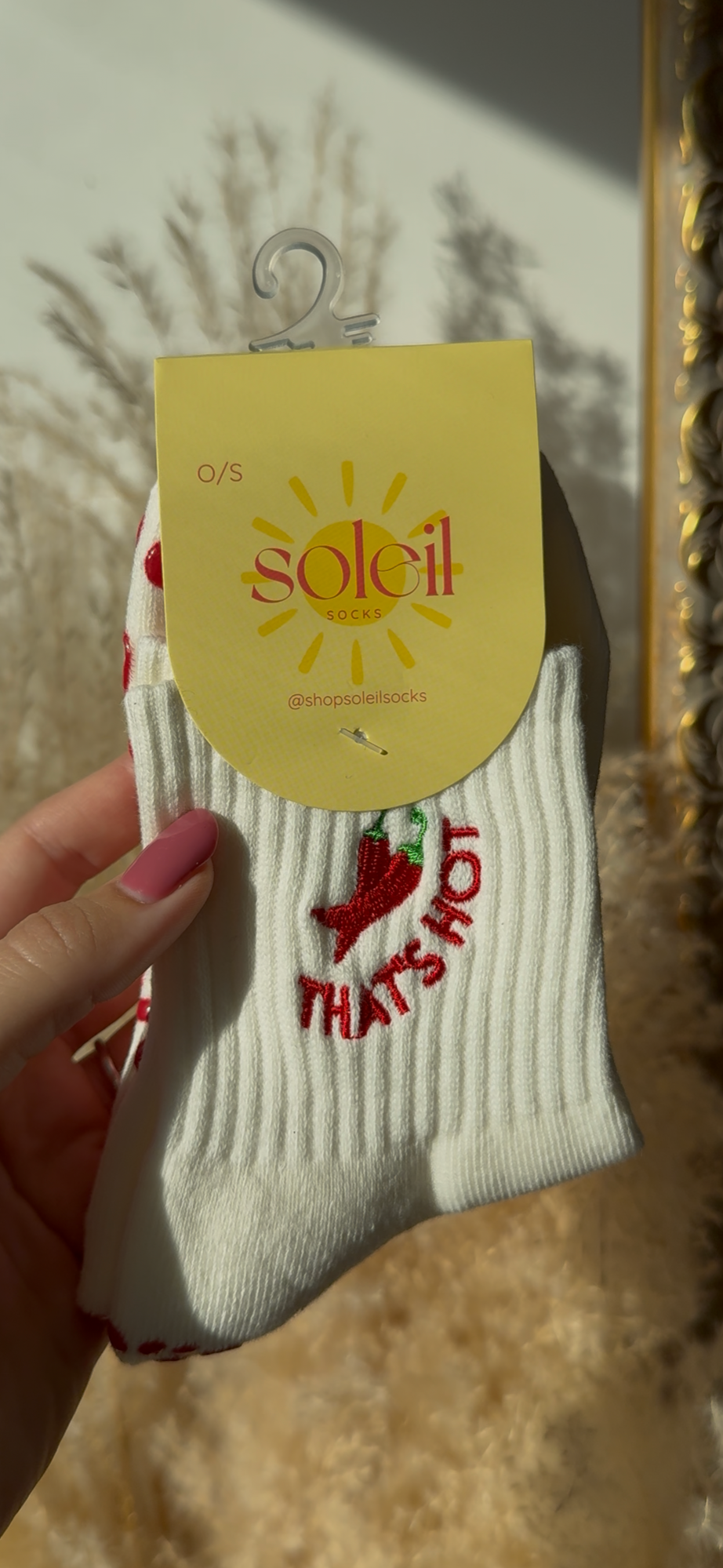 White sock with red text and chili "that's hot" text design held by a hand, on a 'soleil' branded tag.