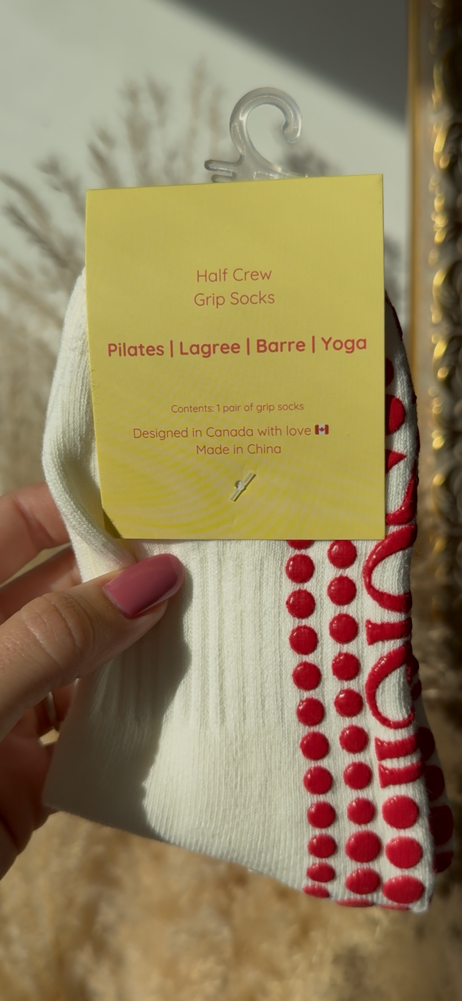 Hand holding a white sock with a red pattern against a decorative mirror background