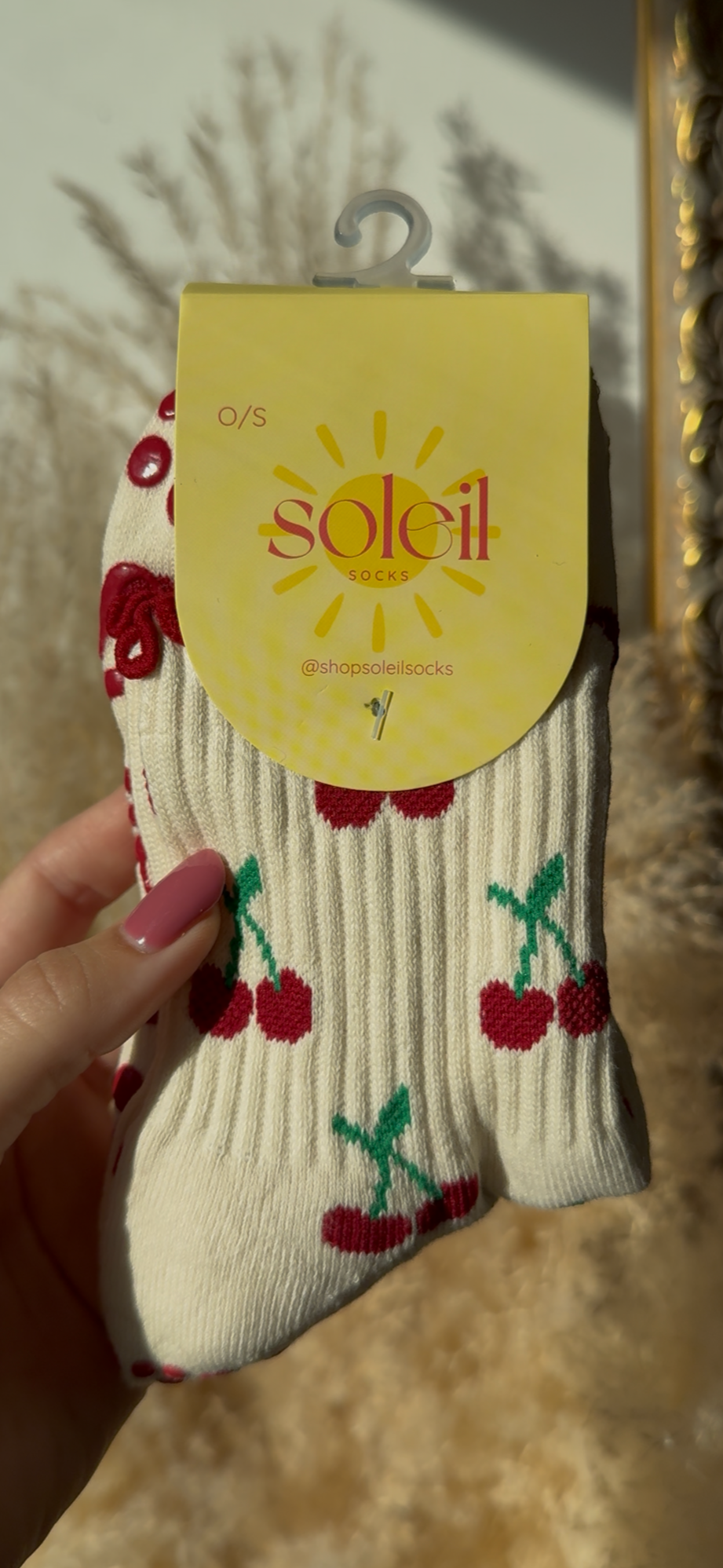 White sock with red cherries held by a hand, against a neutral background